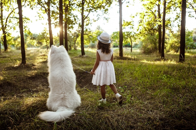 Young girl walking, playing with dog in park at sunset.