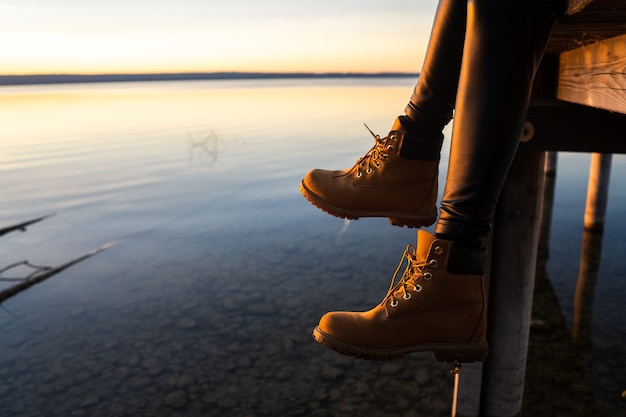 Young girl wearing boots sitting on a pier during sunset