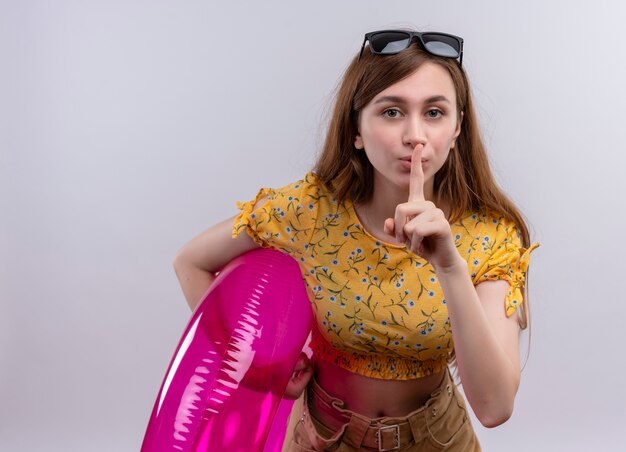 Young girl wearing sunglasses on head holding swim ring and gesturing silence  on isolated white wall