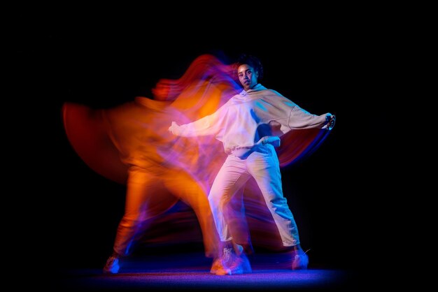 Young girl in white hoodie dancing hip-hop isolated over black background in neon with mixed lights