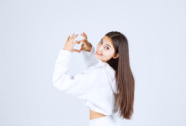 young girl in white hoodie showing heart with two hands.