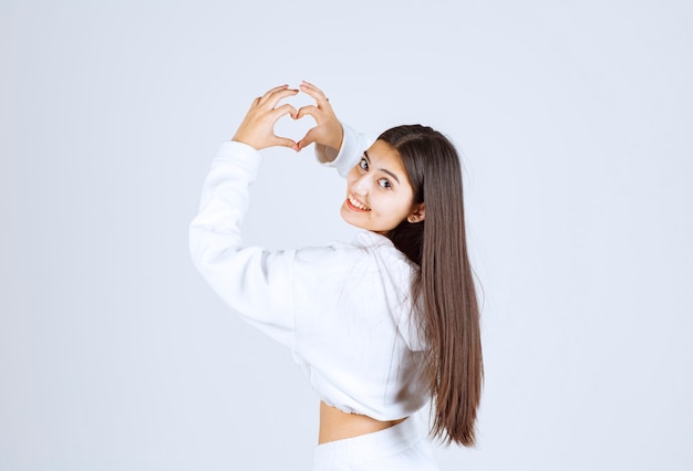 Giovane ragazza in felpa con cappuccio bianca che mostra il cuore con due mani.