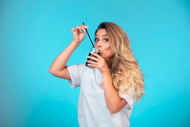 Young girl in white shirt drinking a glass of black cocktail.