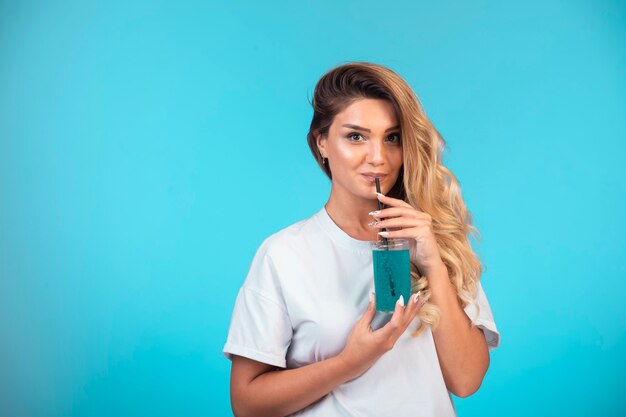 Young girl in white shirt drinking a glass of blue cocktail.