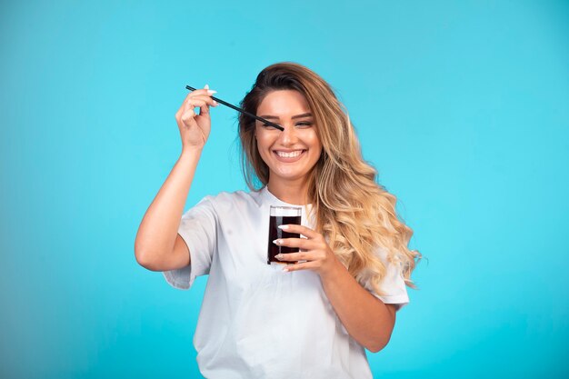 Young girl in white shirt holding a glass of black cocktail and checking the taste.