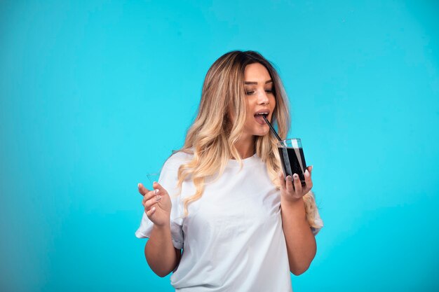 Young girl in white shirt holding a glass of black cocktail and drinking it.