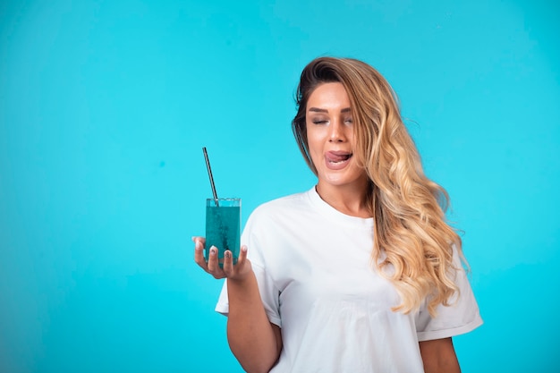 Young girl in white shirt holding a glass of blue cocktail and feels the taste. 