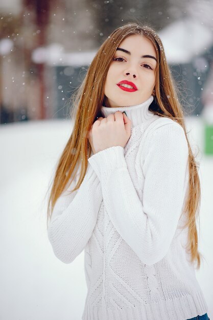 Молодая девушка в белом свитере стоит в зимнем парке