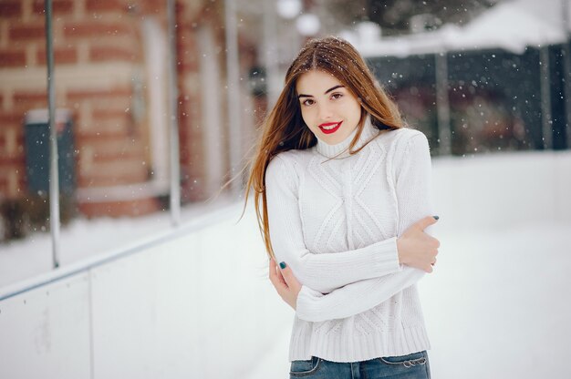 Молодая девушка в белом свитере стоит в зимнем парке