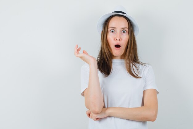 Young girl in white t-shirt, hat and looking amazed , front view.