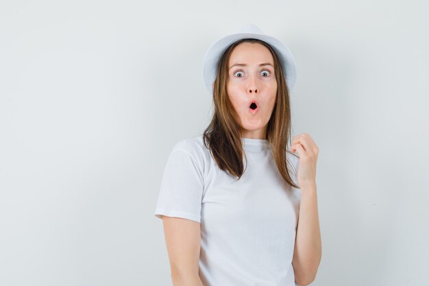 Young girl in white t-shirt, hat and looking surprised , front view.