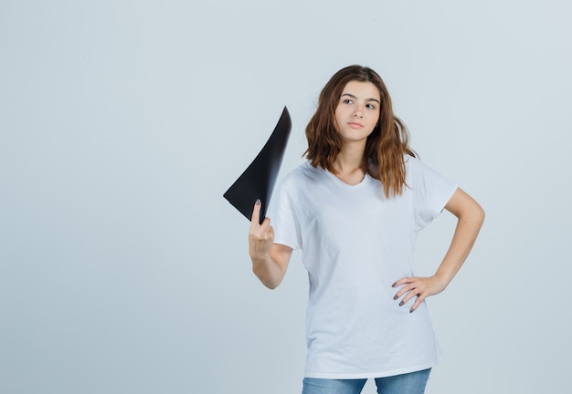 Young girl in white t-shirt holding folder and looking pensive , front view.