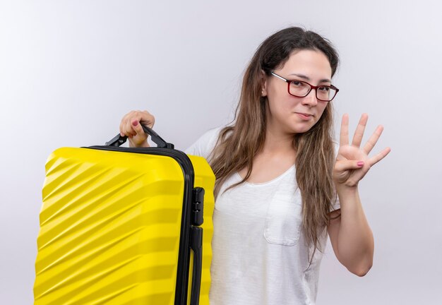 Young girl in white t-shirt holding travel suitcase  showing and pointing up with fingers number three smiling 