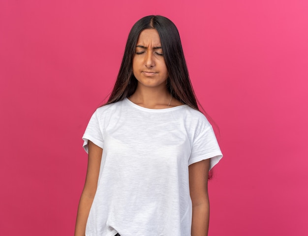 Young girl in white t-shirt looking annoyed and irritated standing over pink