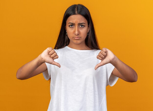 オレンジ色の上に立って親指を下に見せて不機嫌にカメラを見ている白いTシャツの少女