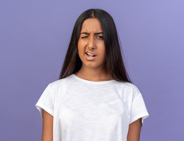 Young girl in white t-shirt looking at camera confused and displeased winking 