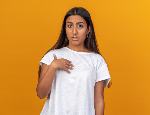 Young girl in white t-shirt looking at camera confused pointing at herself 