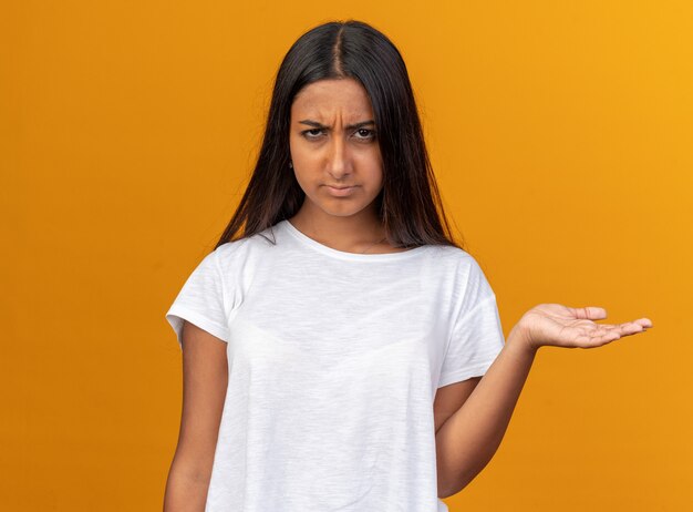 Young girl in white t-shirt looking at camera confused raising arm in displeasure and indignation 