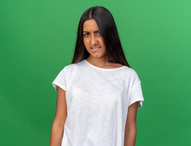 Young girl in white t-shirt looking at camera making wry mouth with disappointed expression 