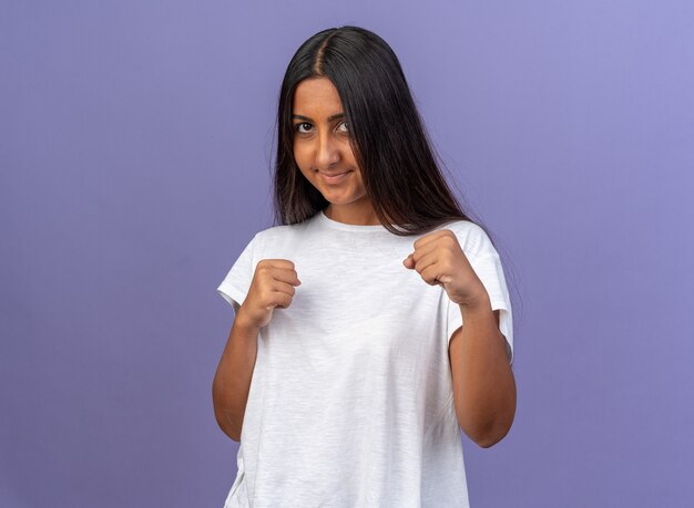 Young girl in white t-shirt looking at camera with clenched fists smiling with happy face 