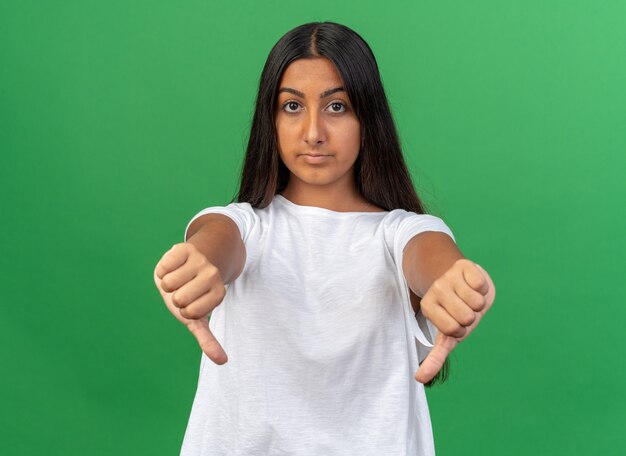 Young girl in white t-shirt looking at camera with serious face showing thumbs down 