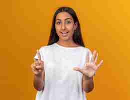 Free photo young girl in white t-shirt looking at camera with smile on face showing and pointing up with fingers number six