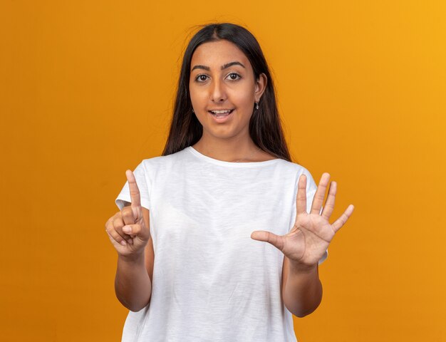 Young girl in white t-shirt looking at camera with smile on face showing and pointing up with fingers number six 