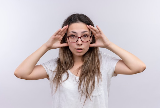 Young girl in white t-shirt opening eyes with hands trying to see better 