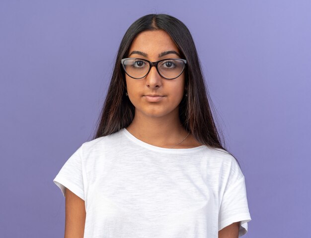 Young girl in white t-shirt wearing glasses looking at camera with serious confident expression 