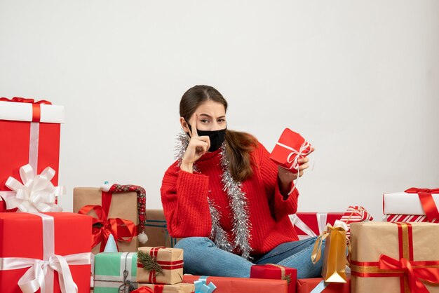young girl with black mask holding her gift sitting around presents on white