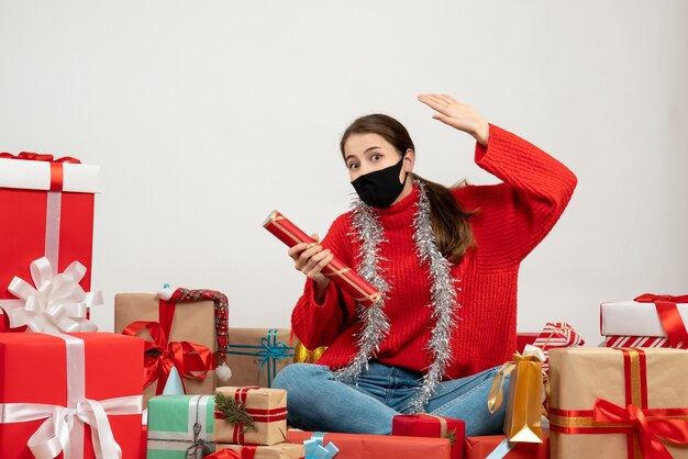 young girl with black mask holding party popper sitting around presents on white