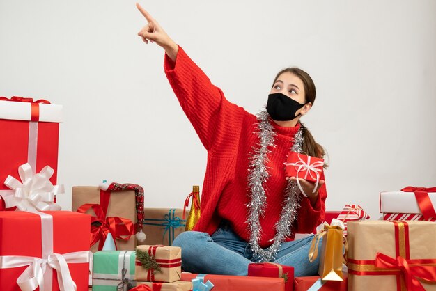 young girl with black mask looking at something sitting around presents on white