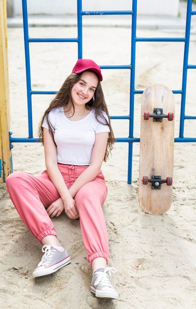 Foto gratuita ragazza con cappuccio seduto accanto a skateboard