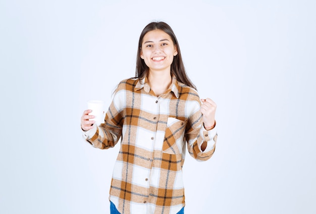 Giovane ragazza con una tazza di tè sentirsi allegra sul muro bianco.