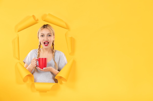 Giovane ragazza con una tazza di tè su carta gialla strappata sfondo pubblicità shopping facciale