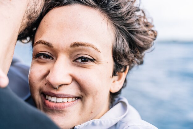 Young girl with curly hair looking straight ahead as she embraces her partner with the unfocused sea