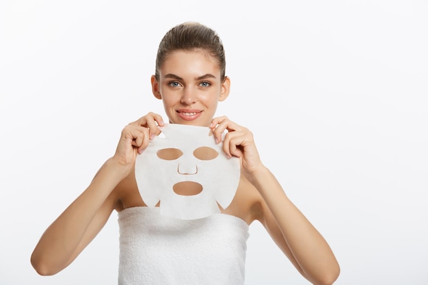 Бесплатное фото Молодая девушка с маской для лица смотрит в камеру на белом фоне косметическая процедура салон красоты спа