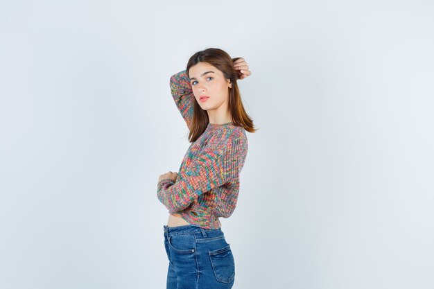 Молодая девушка с рукой за головой, глядя через плечо в трикотаж, джинсы и выглядя заманчиво, вид спереди.