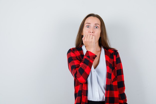 Young girl with hand on mouth in checkered shirt, blouse and looking scared , front view.