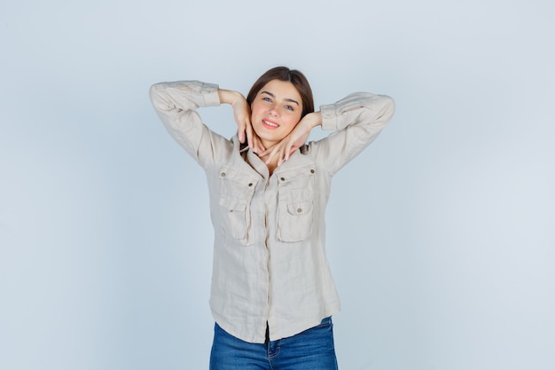 Young girl with hands under chin in beige shirt, jeans and looking cute. front view.