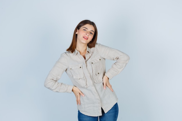 Free photo young girl with hands on hips in beige shirt, jeans and looking cute , front view.