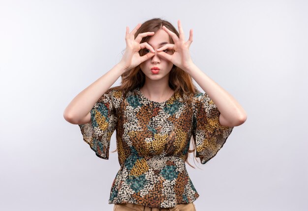 Young girl with long hair wearing colorful dress doing ok signs with fingers like binoculars looking through fingers 