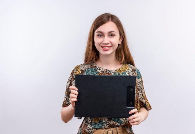 Young girl with long hair wearing colorful dress holding clipboard looking at camera smiling happy and positive 