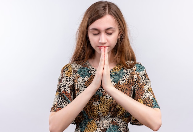 Foto gratuita giovane ragazza con i capelli lunghi che indossa abiti colorati che tengono le mani in preghiera namaste gesto, sentendosi grati e felici con gli occhi chiusi