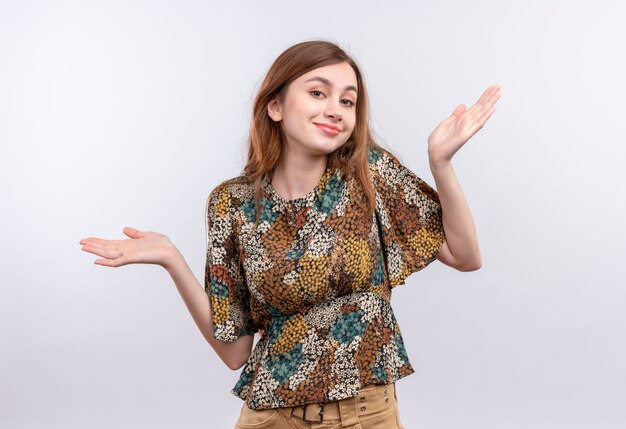 Young girl with long hair wearing colorful dress smiling cheerfully spreading arms to the sides, having no answer 