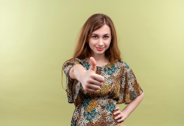 Young girl with long hair wearing colorful dress smiling confident showing thumbs up  