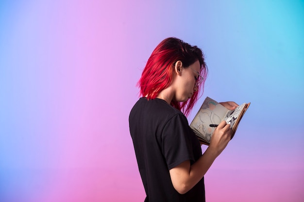 Бесплатное фото Молодая девушка с розовыми волосами держит альбом для рисования и смотрит.