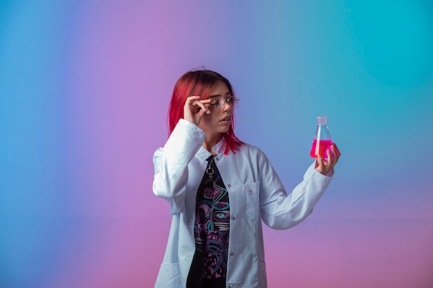 Ragazza con i capelli rosa che tiene una boccetta chimica e guarda attentamente.