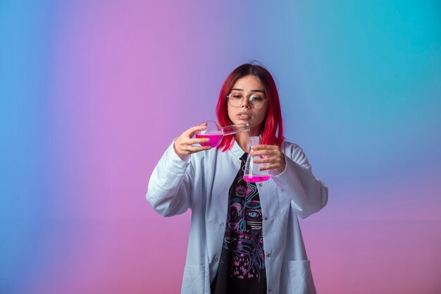 Young girl with pink hairs holding chemical flasks and making reaction. 