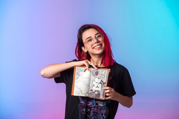 Young girl with pink hairs holding a sketchbook and demonstrating it. 